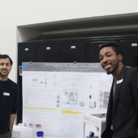 Two students smiling next to a trifold presentation.